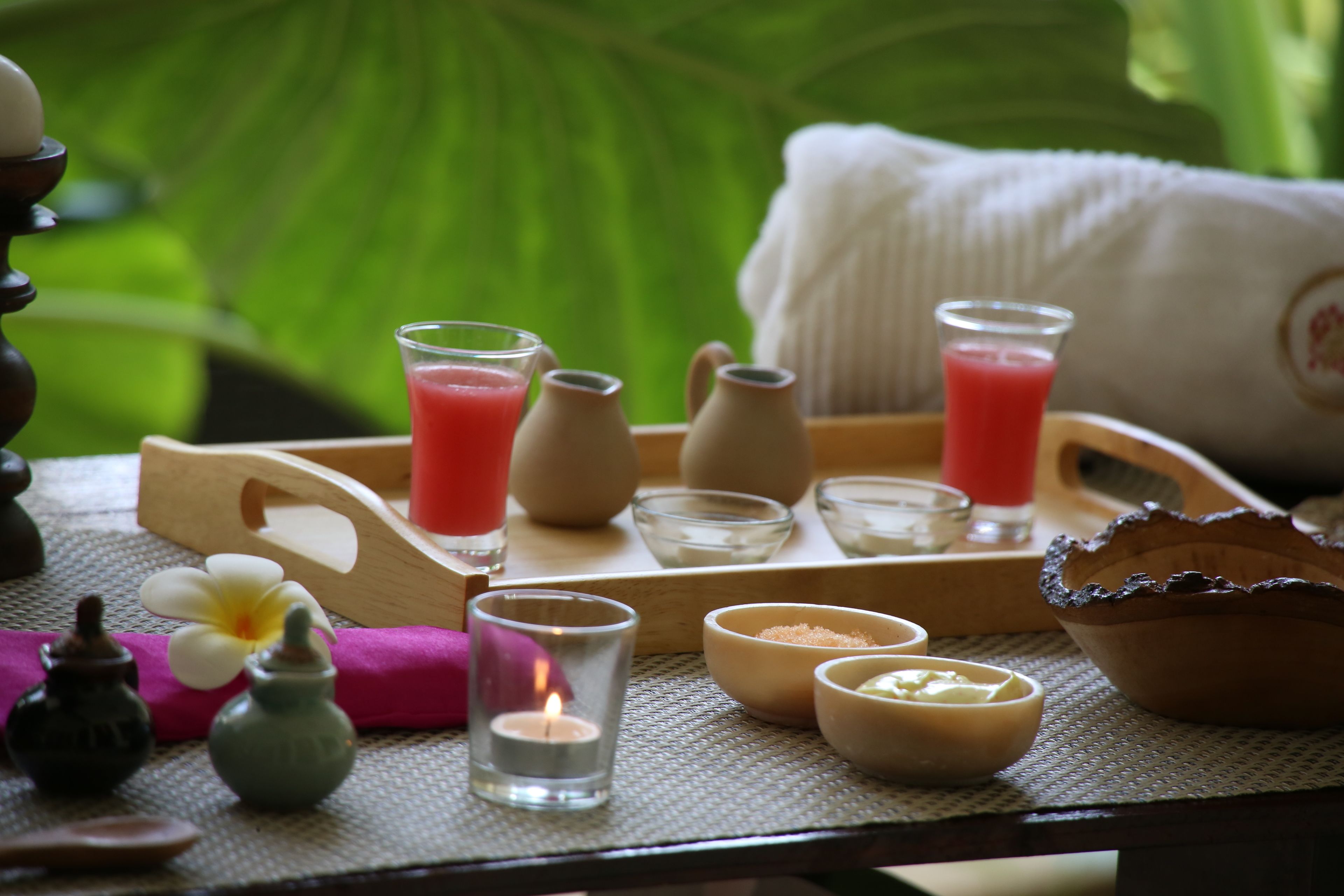 A tray with a pink drink, candles, and small bowls on a table with a green background.
