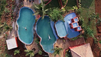 An aerial view of a property with multiple swimming pools, surrounded by lush greenery and a small building.