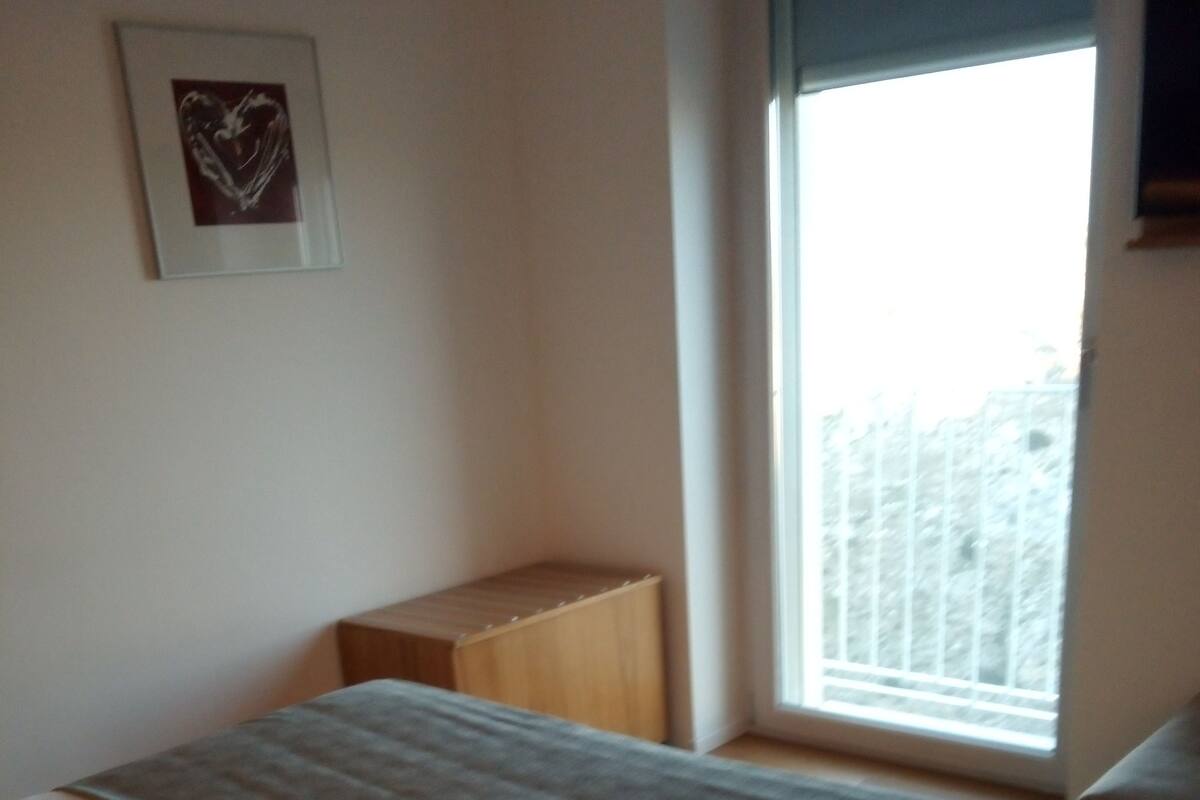 A bedroom with a bed, a window, and a small wooden stool.