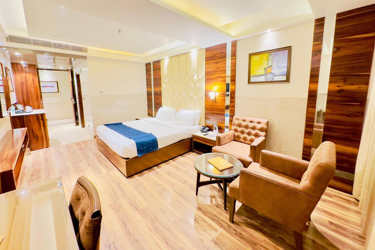 Habitación de hotel moderna con una cama grande, una zona de estar con sofá y sillón, una mesita y un escritorio con silla.
