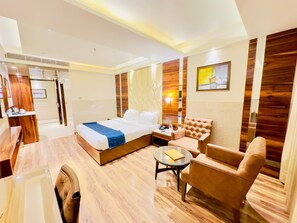 A modern hotel room with a large bed, a sitting area with a sofa and armchair, a small table, and a desk with a chair. - Hotel Vintage (Dera Bassi)