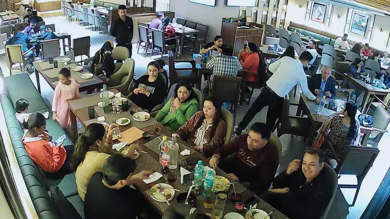 Een levendig restaurant met meerdere tafels en stoelen, mensen aan het dineren, en diverse tafelopstellingen met borden, bekers en flessen.