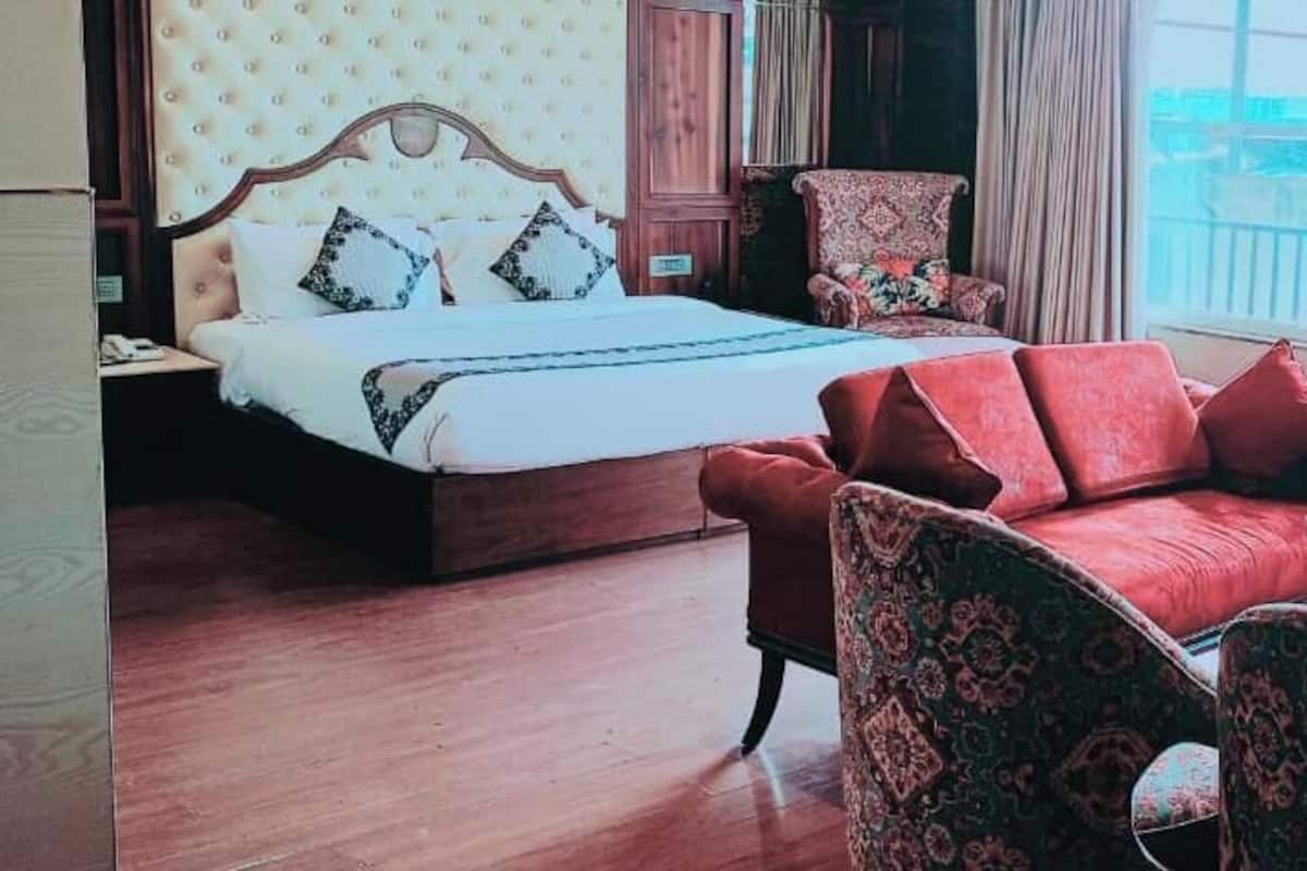 Una habitación de hotel con una cama, dos sofás rojos, un sillón estampado y vistas a la ciudad.
