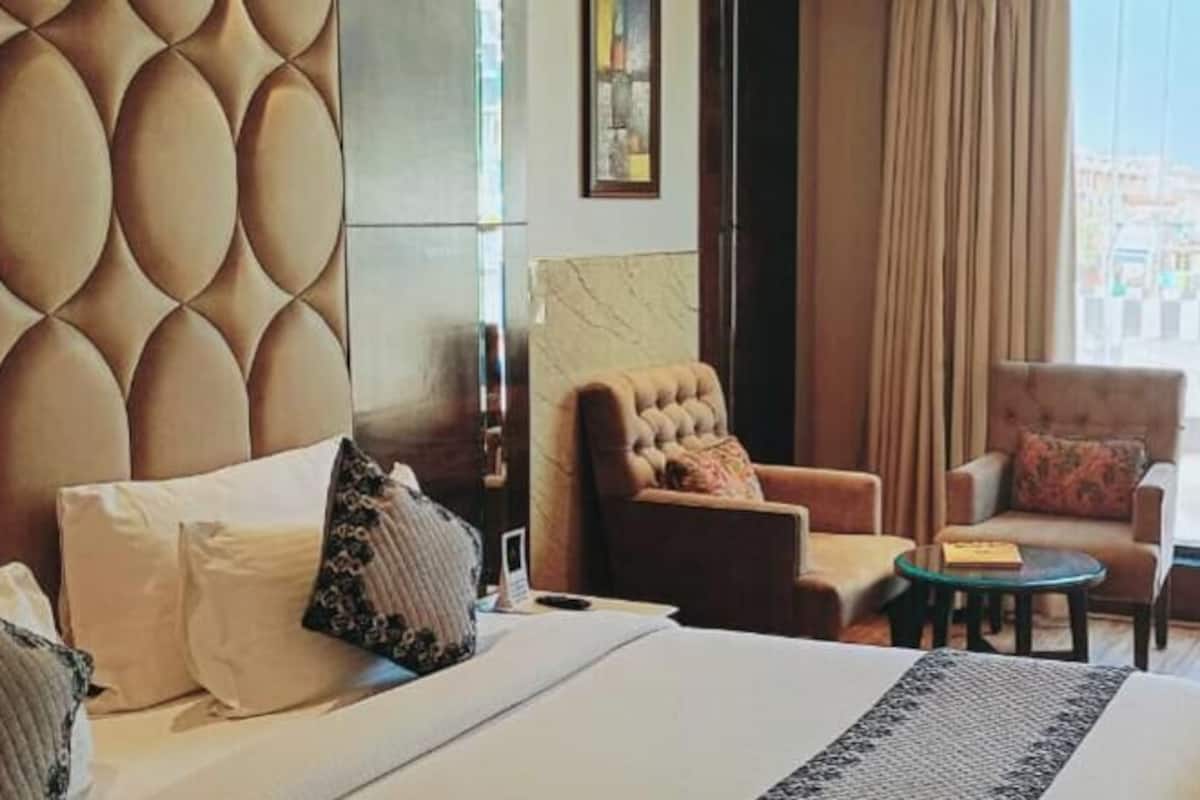 Une chambre d’hôtel comprenant un lit, deux fauteuils, une petite table, un bureau et une vue sur l’extérieur.