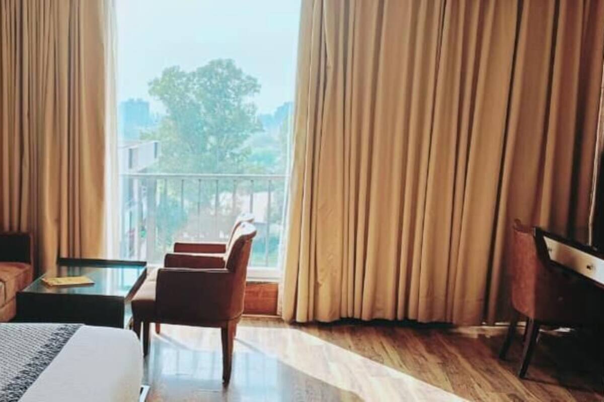 Una habitación de hotel con cama, sofá, sillón, una mesita y vistas al exterior.