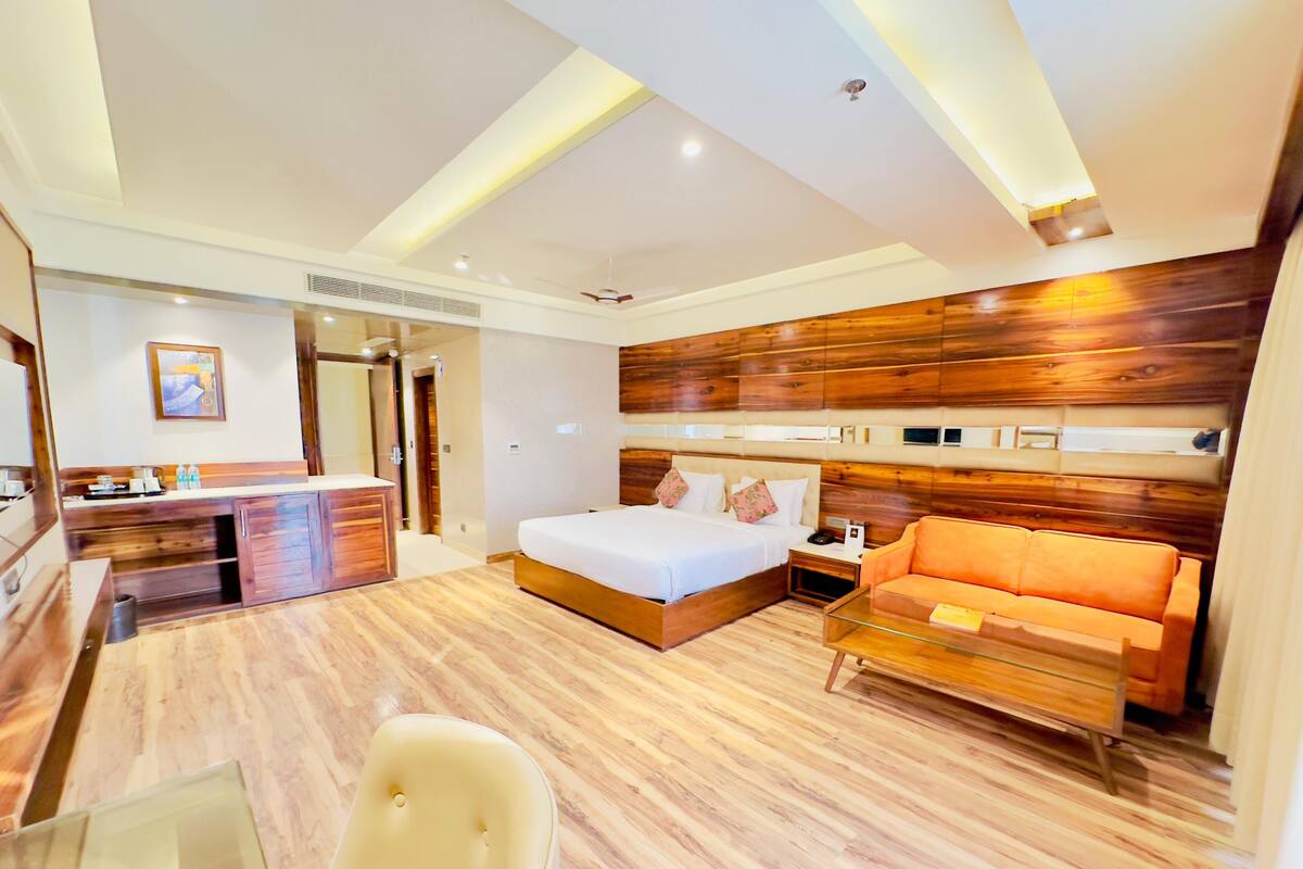 A modern hotel room with a wooden floor, a large bed, a sofa, a desk, and a chair.