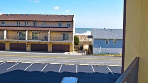 Un edificio de varios pisos con un estacionamiento al frente, una caseta pequeña y vista al océano.