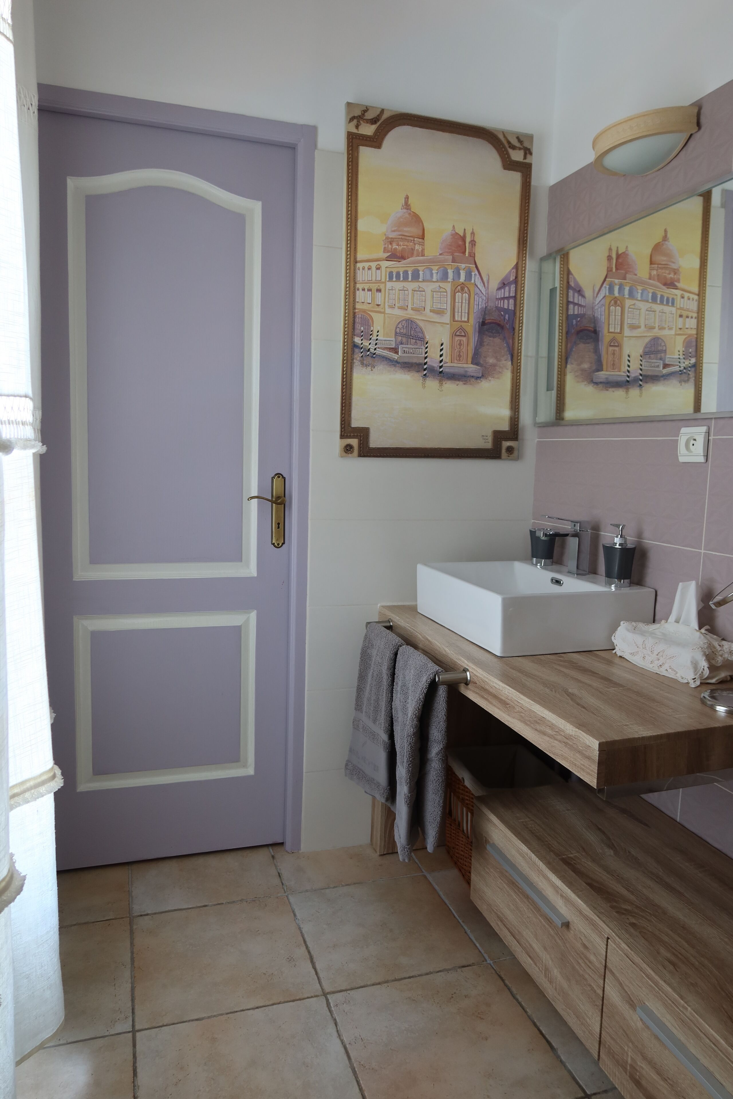 Une salle de bain avec une porte violette, un lavabo blanc et un miroir au-dessus.