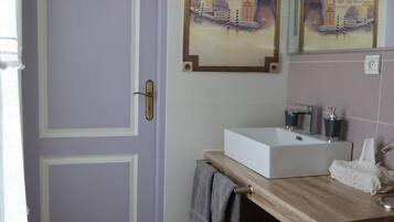 Une salle de bain avec une porte violette, un lavabo blanc et un miroir au-dessus.