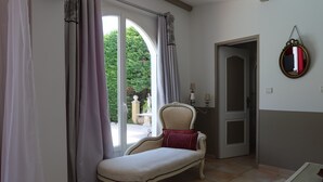 A room with a chaise lounge near a window, a door, and a mirror on the wall.