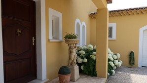 A yellow building with a brown door, a potted plant, and white flowers.