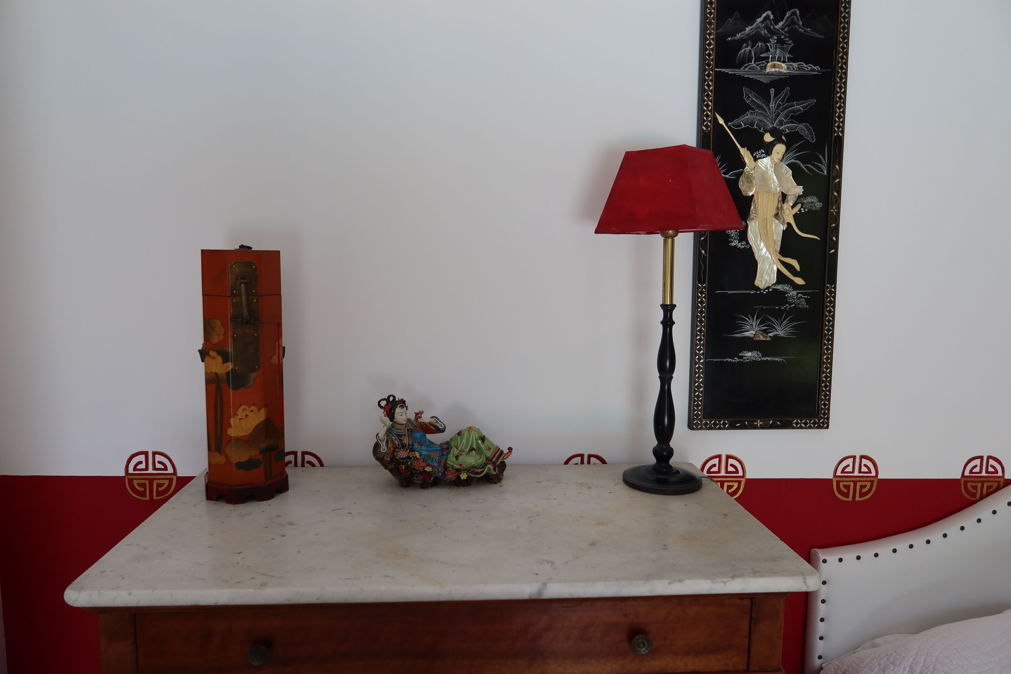 Una habitación con un armario de madera, una lámpara roja, un adorno y una pared con una obra de arte enmarcada.