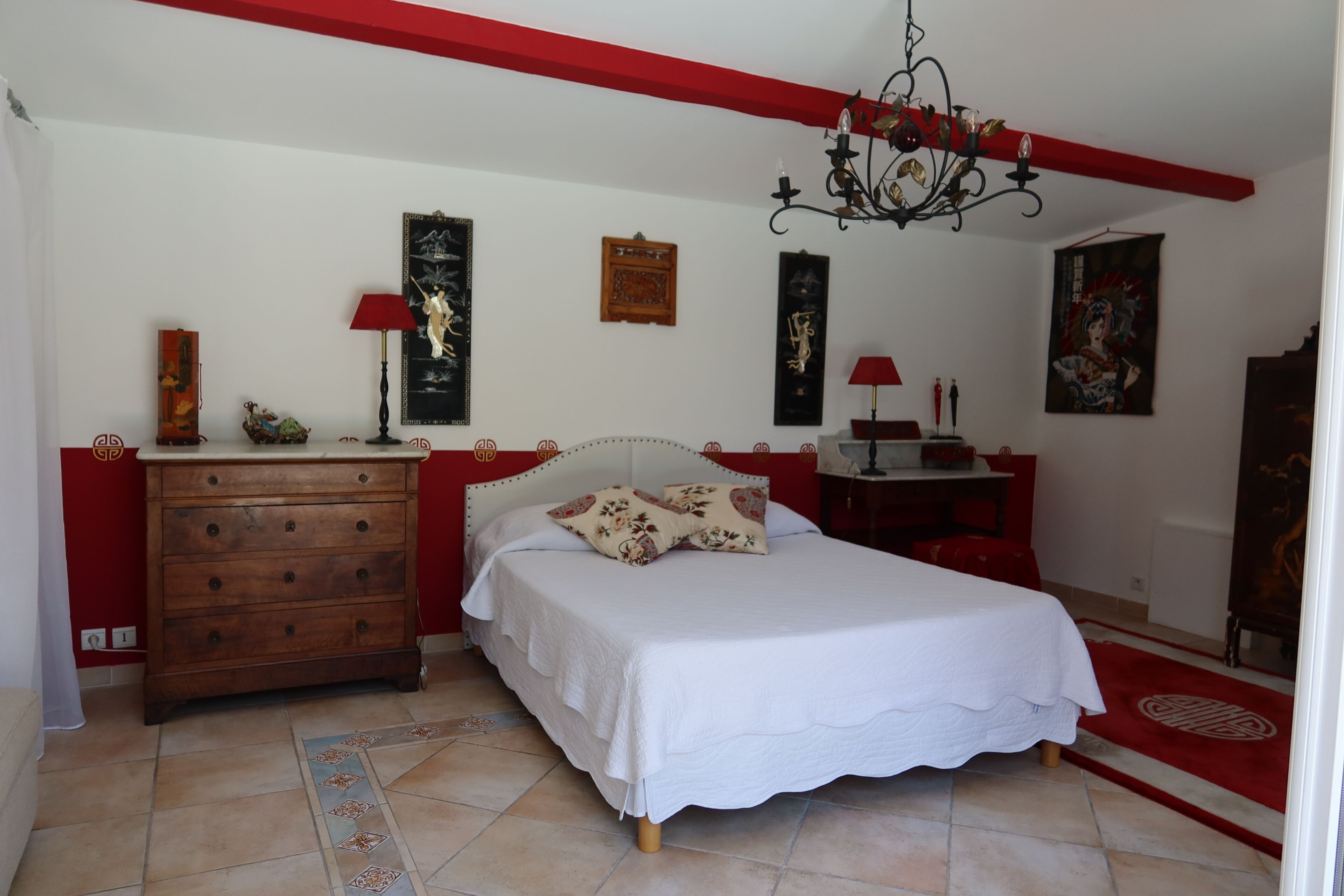 A bedroom with a bed, dresser, and a chandelier.