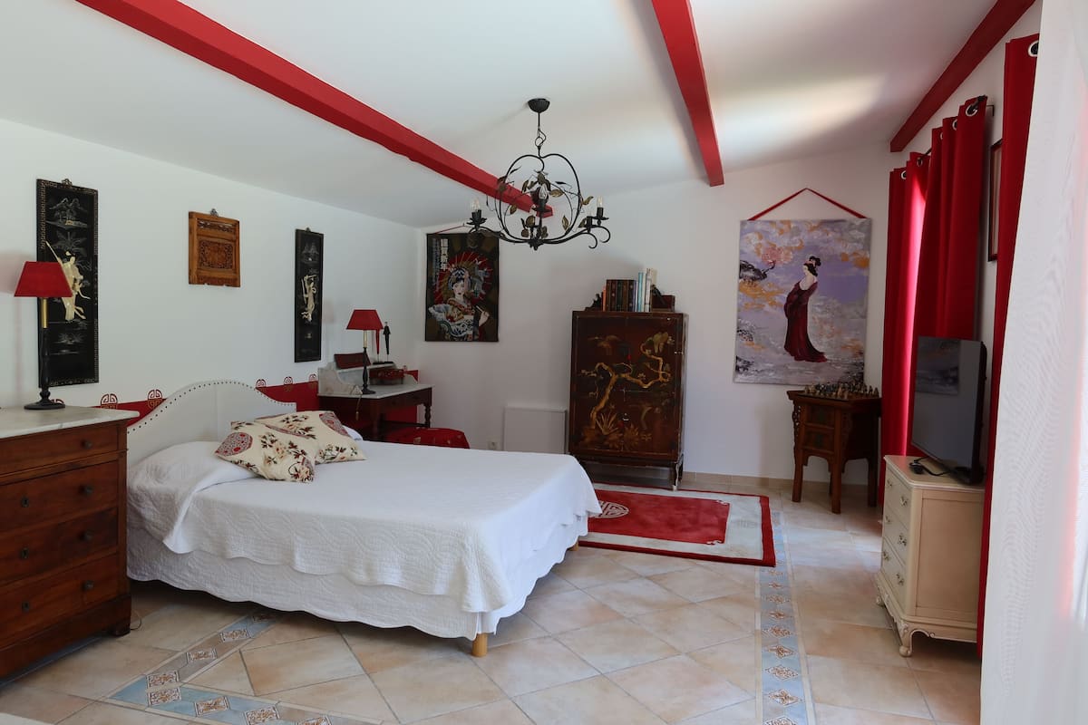 A bedroom with a bed, dresser, TV, and artwork on the walls.