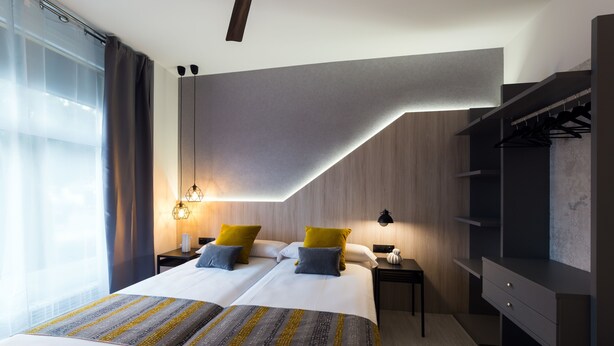 A modern hotel room with two beds, a wardrobe, and a nightstand with a lamp. - Hotel Onyarbi (Hondarribia)