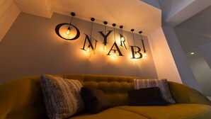 A modern living room with a yellow sofa, patterned cushions, and a wall-mounted light fixture spelling out "ONAB!" with hanging bulbs. - Hotel Onyarbi (Hondarribia)