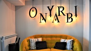 A yellow sofa with patterned cushions against a wall with illuminated letters spelling "ONYRABI". - Hotel Onyarbi (Hondarribia)
