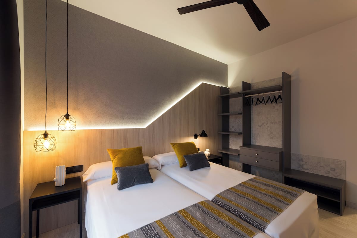 A modern bedroom with a bed, bedside tables, a hanging light fixture, and a built-in shelf.