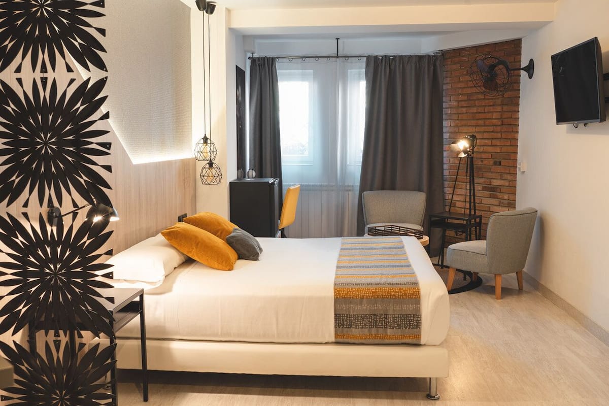 A modern hotel room with a large bed, a desk, a chair, and a TV mounted on the wall.