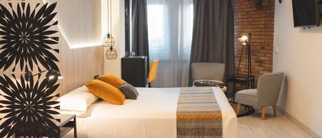 A modern hotel room with a large bed, a desk, a chair, and a TV mounted on the wall.