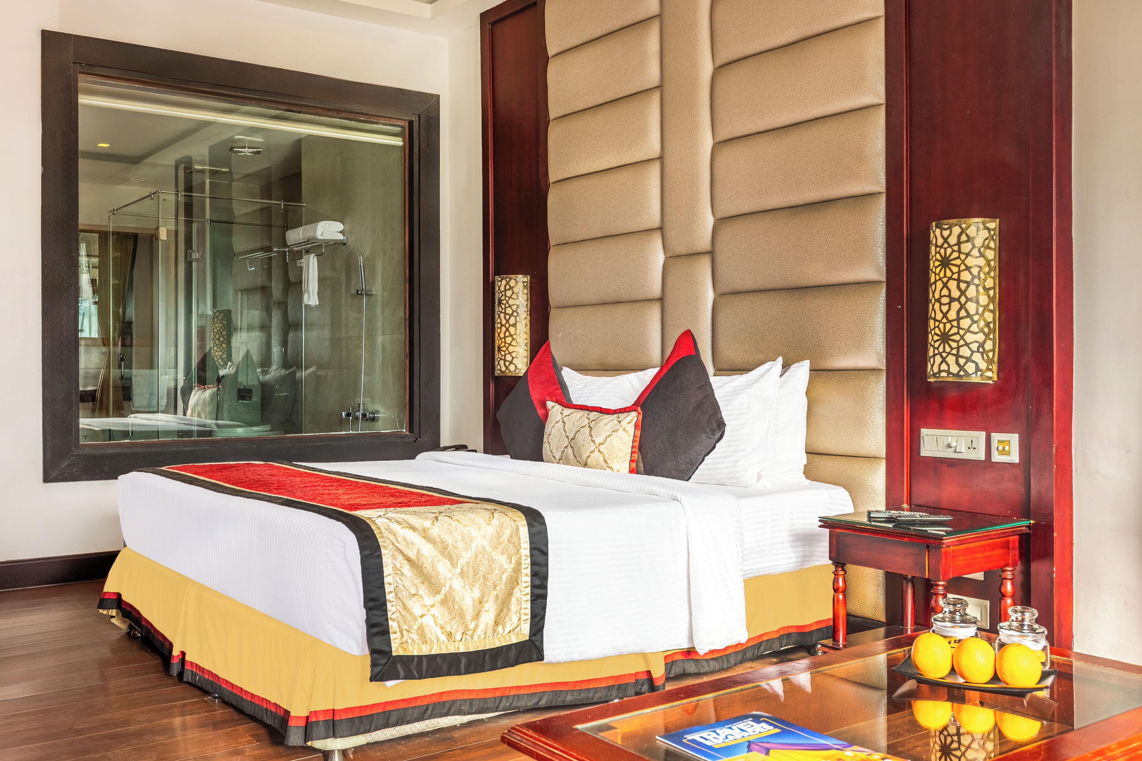 A hotel room with a large bed, a bedside table with a lamp, a mirror, and a view of a bathroom.