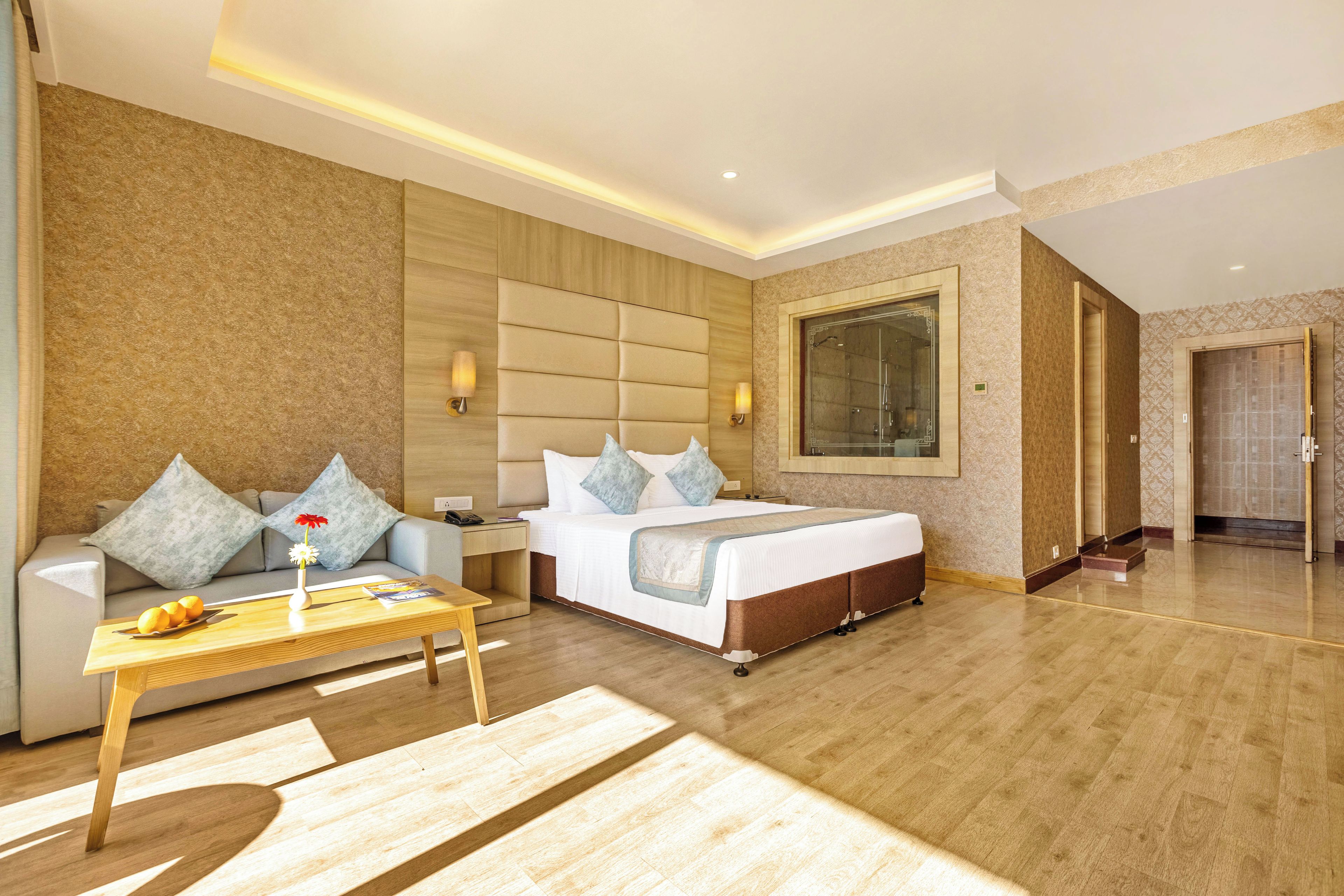 A hotel room with a bed, a sofa, a coffee table, and a large window.