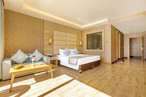 Quarto de hotel com cama, sofá, mesa de centro e uma grande janela.