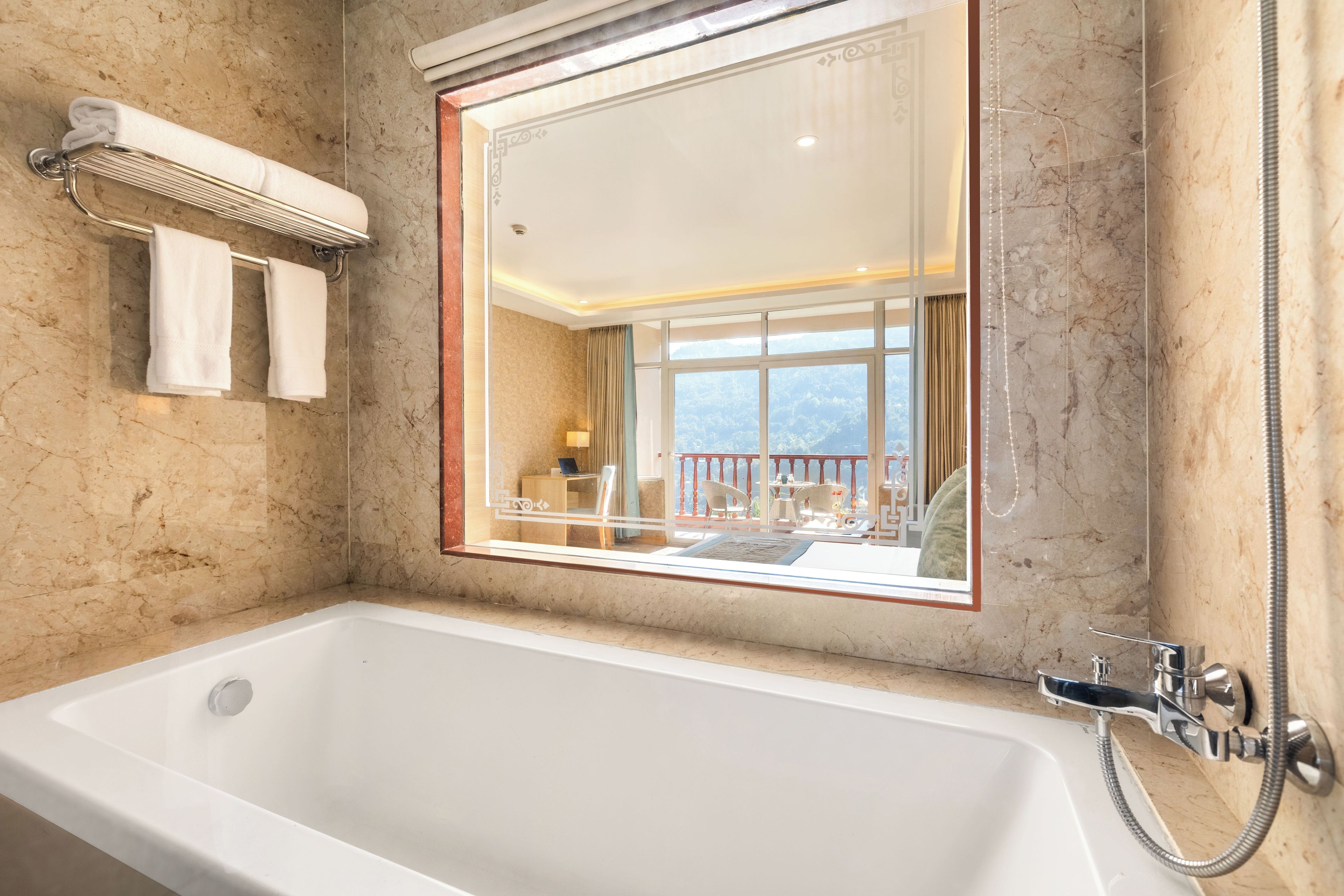 Une salle de bain avec une grande baignoire, un porte-serviettes avec deux serviettes, un miroir qui reflète un balcon aménagé, et un espace douche.
