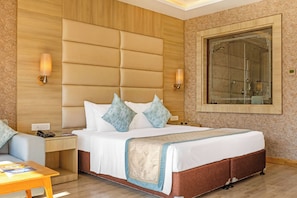 A hotel room with a large bed, a nightstand, a desk, and a bathroom with a glass shower.