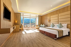 A hotel room with a large bed, a TV, a balcony with a view, and a desk with a chair.