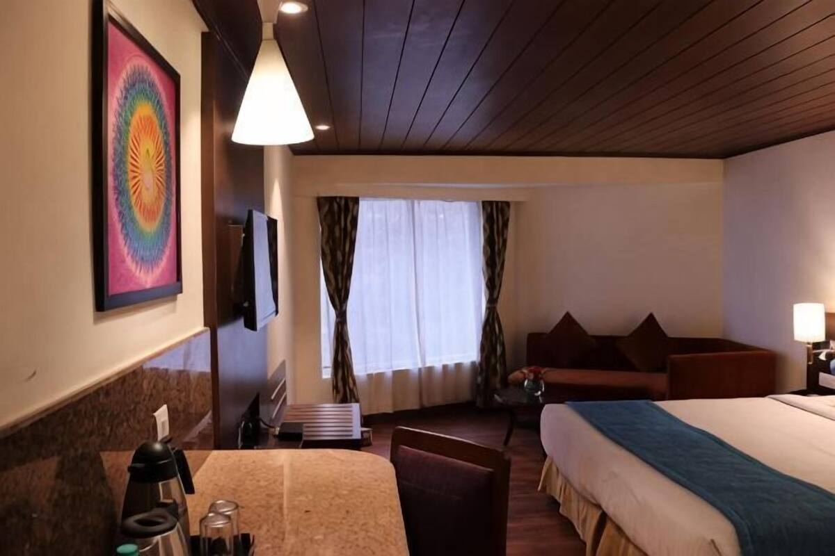 Ein Hotelzimmer mit Bett, Schreibtisch, Stuhl, Fernseher und einem Fenster mit Vorhängen.