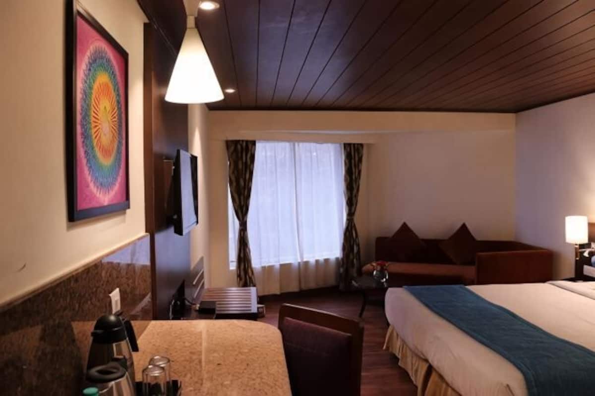 A hotel room with a bed, a desk, a chair, a TV, and a window with curtains.