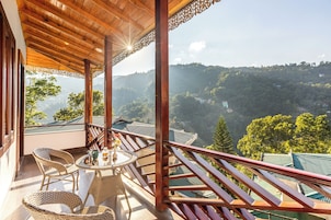 Varanda com móveis de vime, mesa de vidro e vista para uma paisagem montanhosa.
