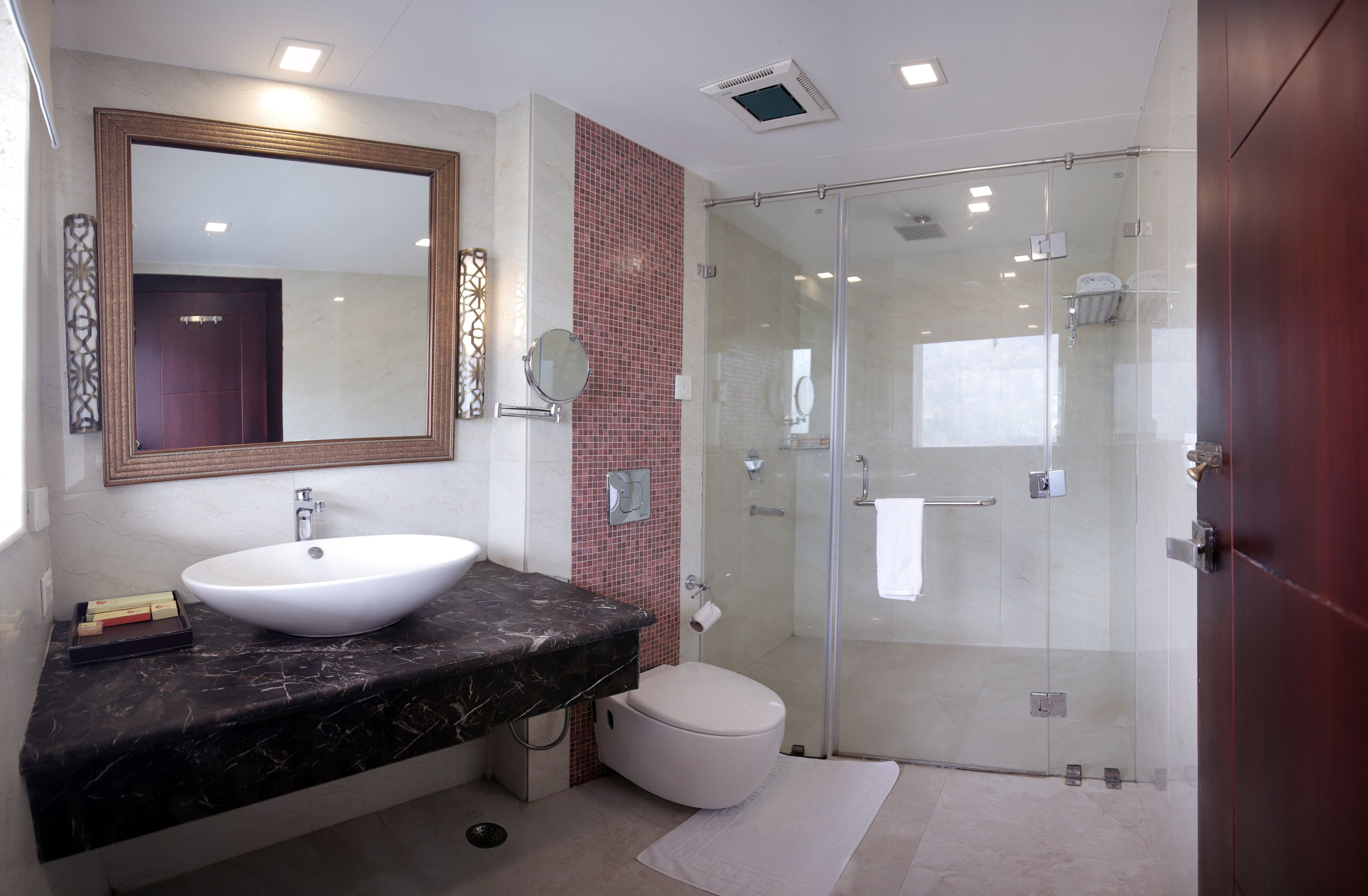 A modern bathroom with a large mirror, a white sink, a toilet, and a glass-enclosed shower.