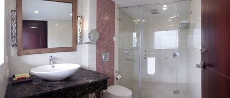 A modern bathroom with a large mirror, a white sink, a toilet, and a glass-enclosed shower.