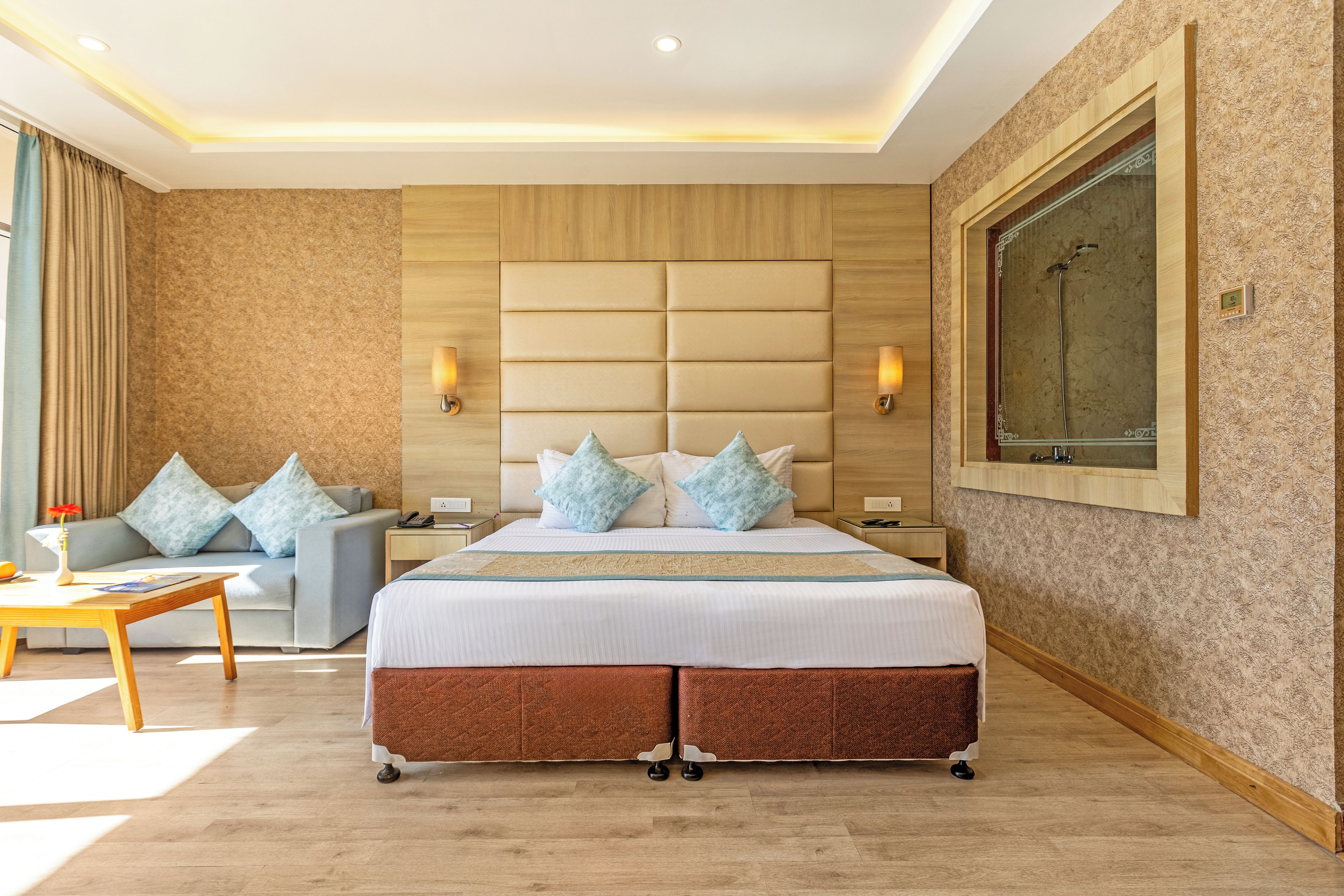 A hotel room with a large bed, a sofa, a nightstand, a desk, and a large window.
