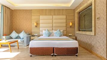 A hotel room with a large bed, a sofa, a nightstand, a desk, and a large window.