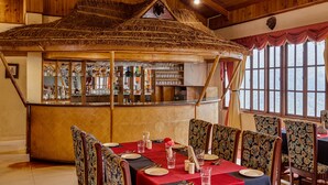 Un restaurant doté d’un bar à toit de chaume, d’un intérieur en bois et offrant une vue sur les montagnes grâce à de grandes fenêtres.