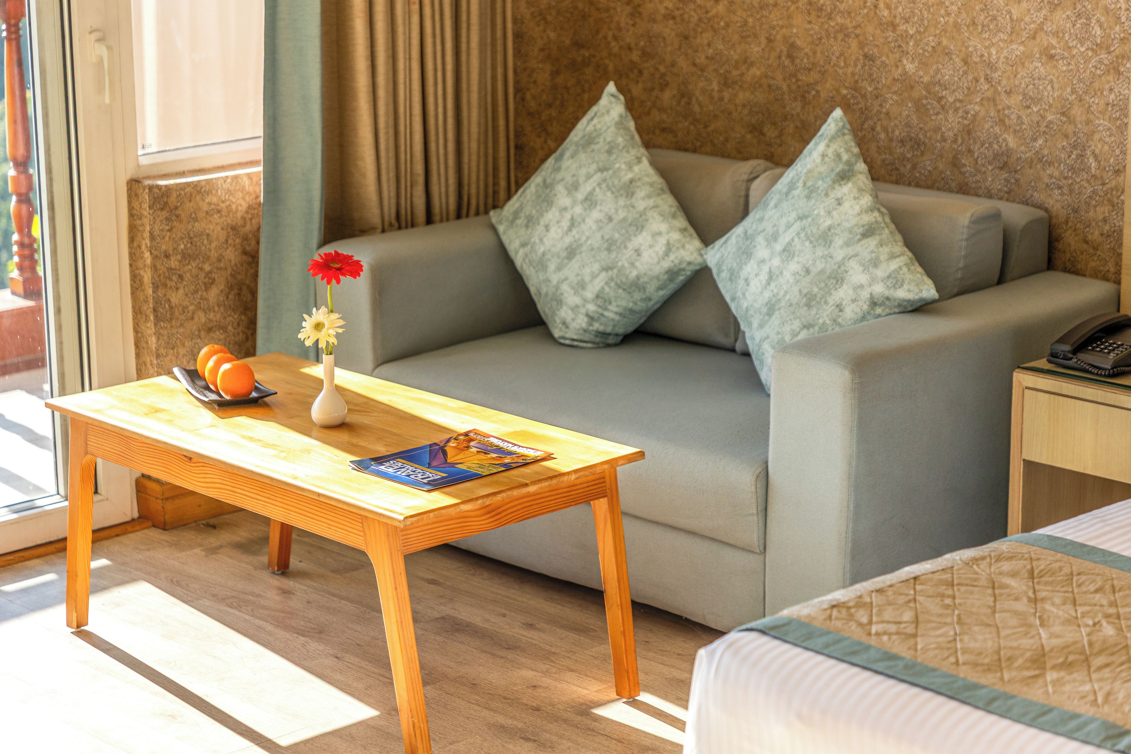 A hotel room with a sofa, a wooden table, a vase with flowers, and a magazine.