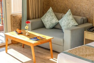 A hotel room with a sofa, a wooden table, a vase with flowers, and a magazine.