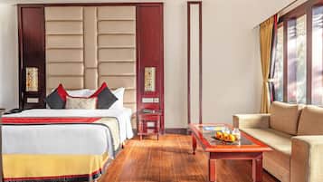 Habitación de hotel con una cama grande, un sofá, una mesita con fruta y un panel decorativo en la pared.