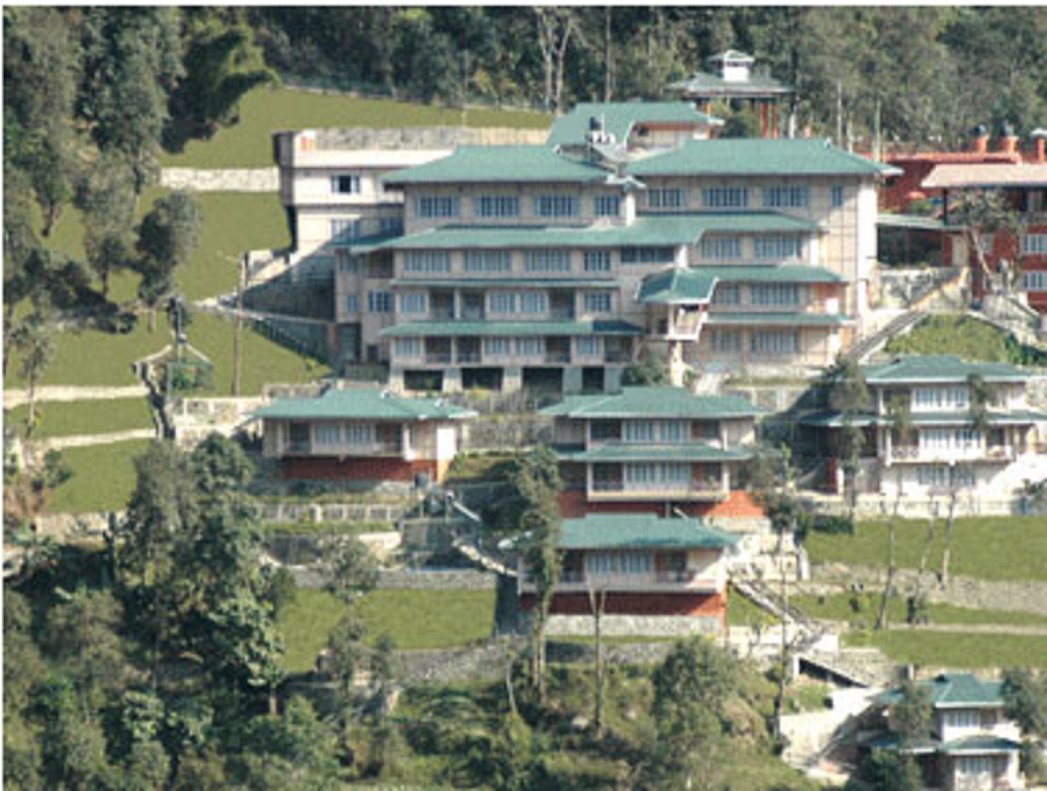 A multi-story building with a green roof, surrounded by greenery and other buildings.