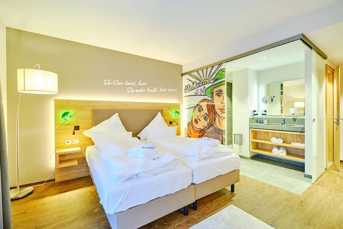 Habitación de hotel con cama, mesita de noche, lámpara y una pared con una cita.