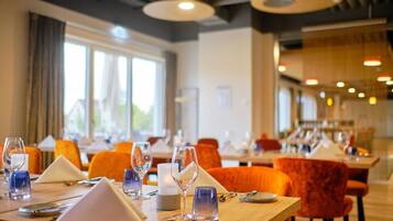 Ein Restaurant mit gedeckten Tischen, orangefarbenen Stühlen und klaren Gläsern.