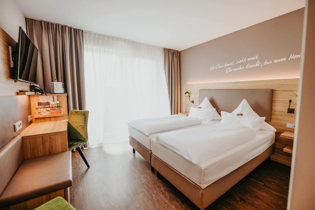 Habitación de hotel con dos camas, un escritorio, una silla, un televisor y una pared con una cita.