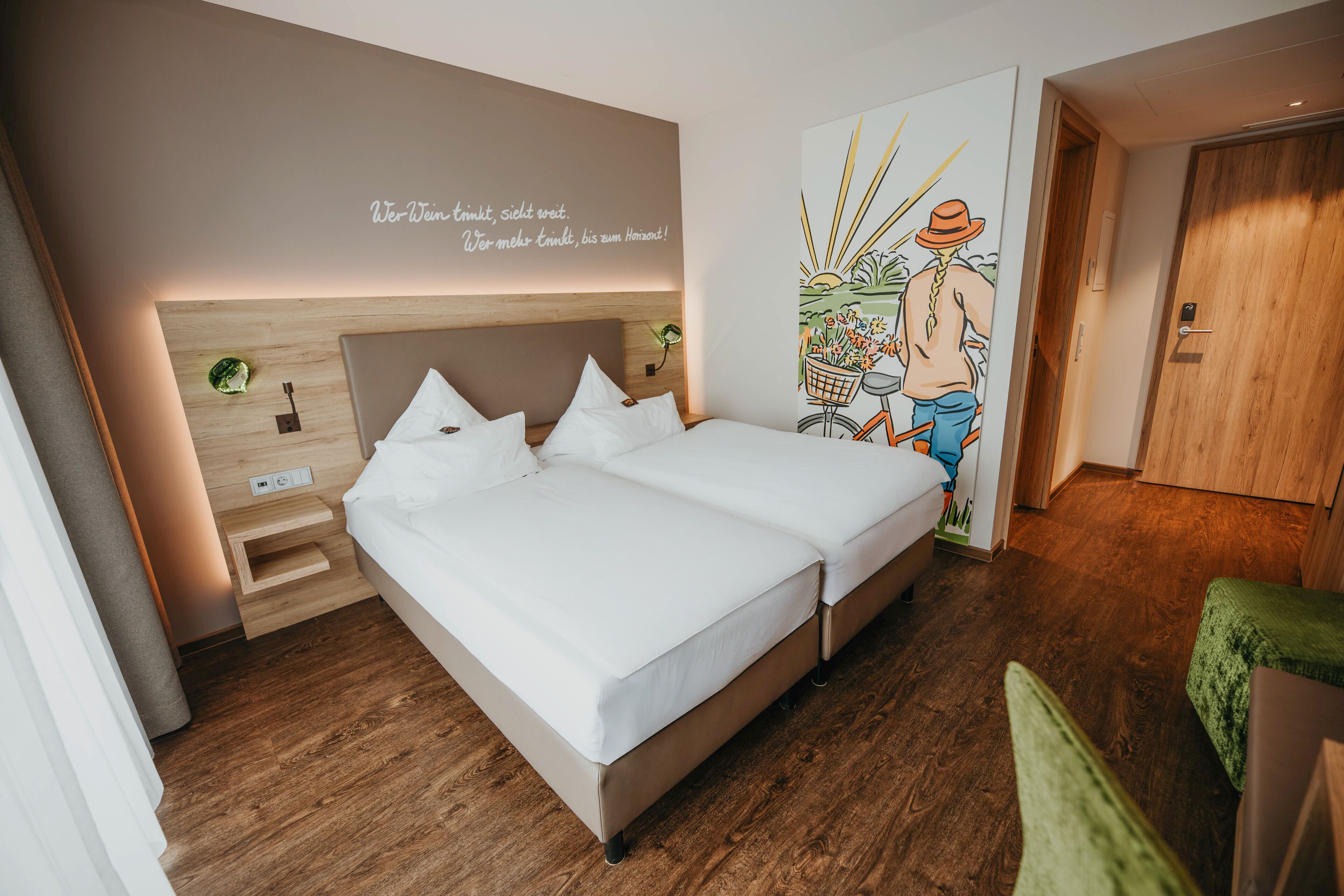 A double bed with a wooden headboard, a bedside table, and a wall with a text and a colorful illustration.