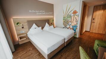 A double bed with a wooden headboard, a bedside table, and a wall with a text and a colorful illustration.