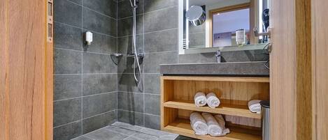 A modern bathroom with a shower, a vanity with a mirror, and a shelf with towels.