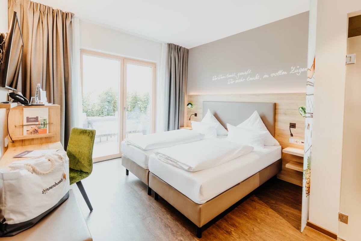 Habitación de hotel con una cama, un escritorio con una silla, un ventanal y una pared con texto.