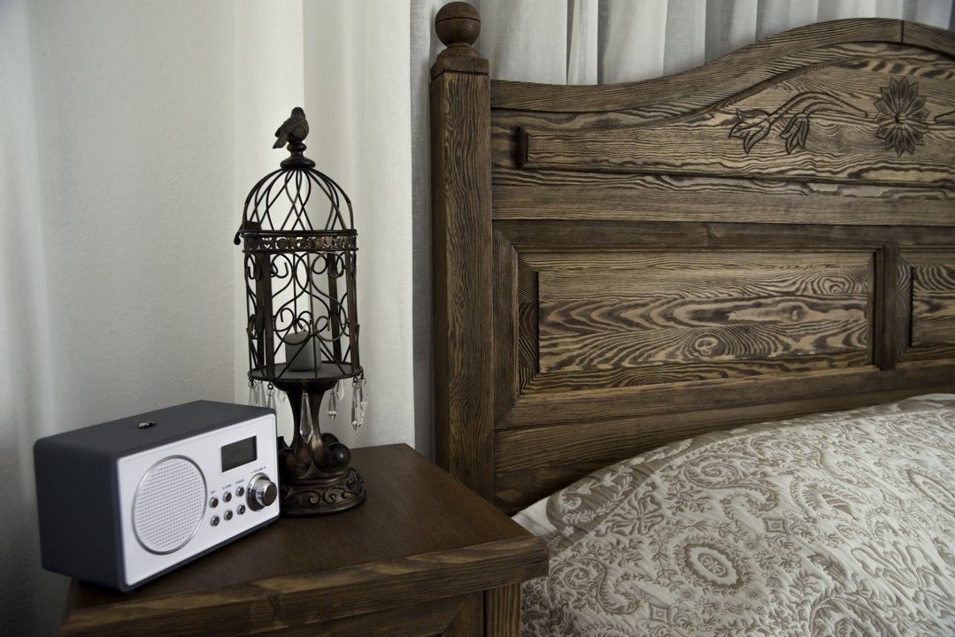 A wooden headboard with a bird and floral design, a radio on a bedside table, and a patterned bedspread.
